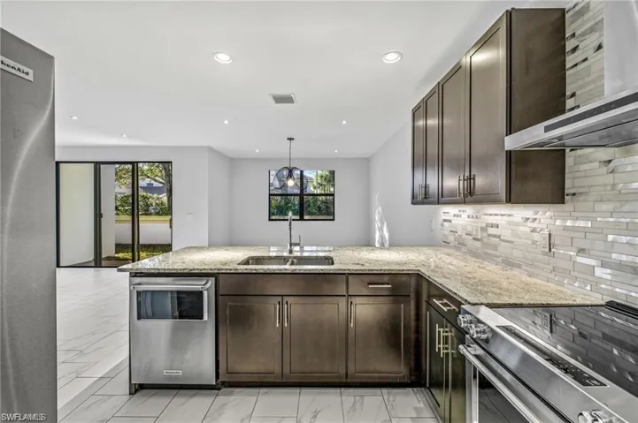Kitchen featuring dark wood finish cabinets, stainless steel appliances, a peninsula, light stone countertops, and light marble finish floors