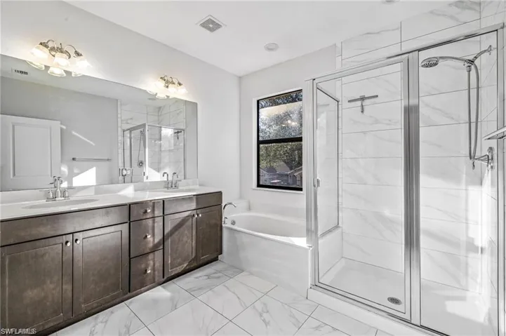 Full bath featuring double vanity, a stall shower, a garden tub, and light marble finish floors