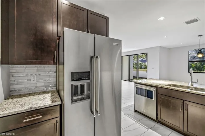 Kitchen with stainless steel appliances, dark wood finish cabinetry, light stone counters, hanging light fixtures, and backsplash