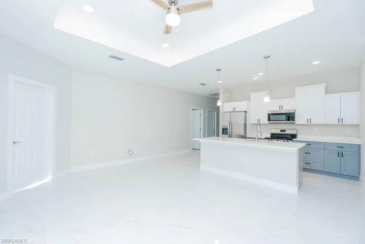 Kitchen with white cabinetry, a tray ceiling, a center island with sink, recessed lighting, and appliances with stainless steel finishes