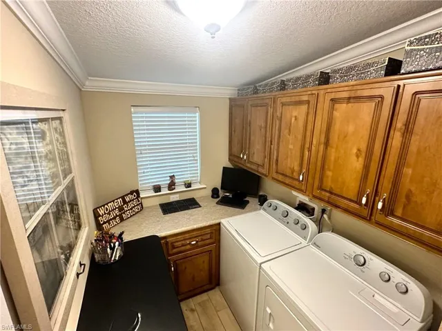 Clothes washing area featuring light hardwood / wood-style floors, independent washer and dryer, a textured ceiling, crown molding, and cabinets