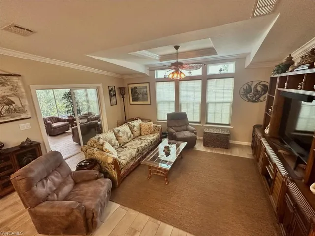 Living room featuring light hardwood / wood-style flooring, a tray ceiling, ceiling fan, and ornamental molding
