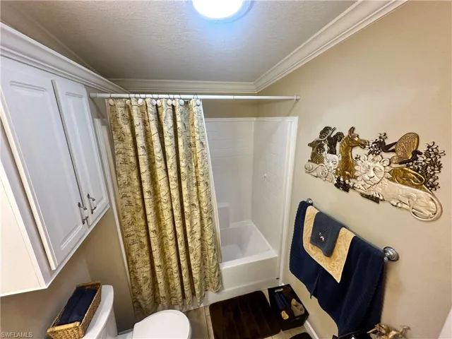 Guest Bathroom featuring shower / tub combo with curtain, a textured ceiling, crown molding, and toilet