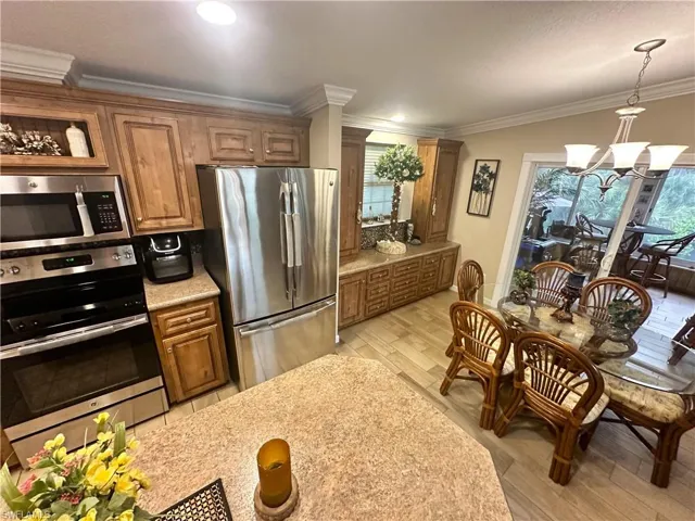 Kitchen featuring hanging light fixtures, light hardwood / wood-style floors, stainless steel appliances, an inviting chandelier, and ornamental molding