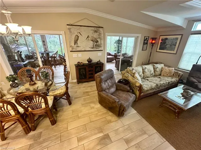 Living room with lofted ceiling, a chandelier, plenty of natural light, and crown molding