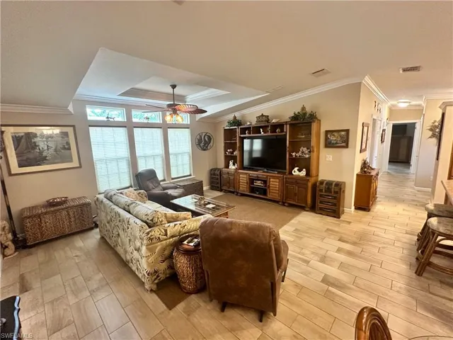 Living room with ceiling fan, light hardwood / wood-style floors, a raised ceiling, and ornamental molding