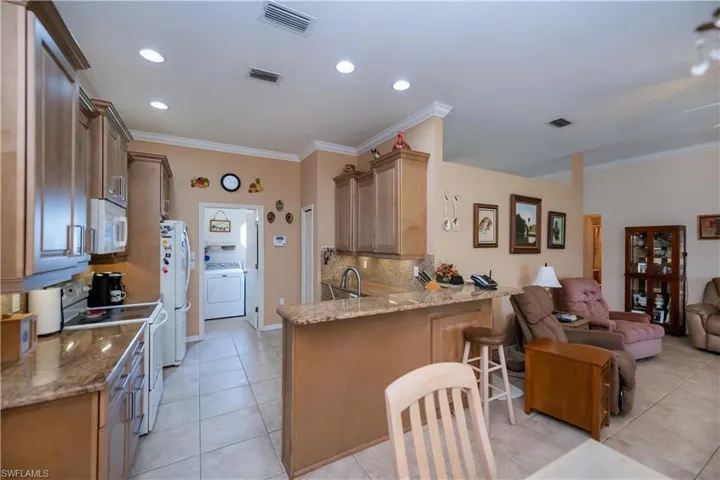 Kitchen with white appliances, washer / dryer, a peninsula, light tile patterned flooring, and open floor plan