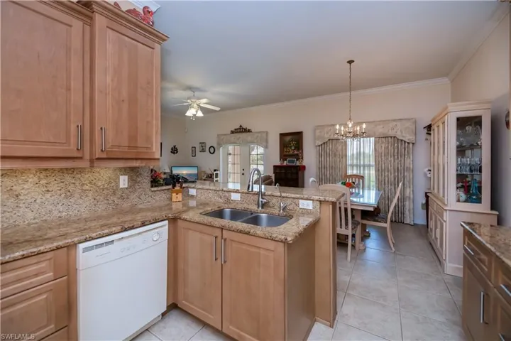 Kitchen featuring dishwasher, a sink, a peninsula, light tile patterned floors, and light brown cabinetry