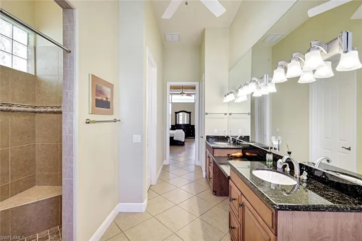 Ensuite bathroom featuring a ceiling fan, double vanity, light tile patterned flooring, and a walk in shower