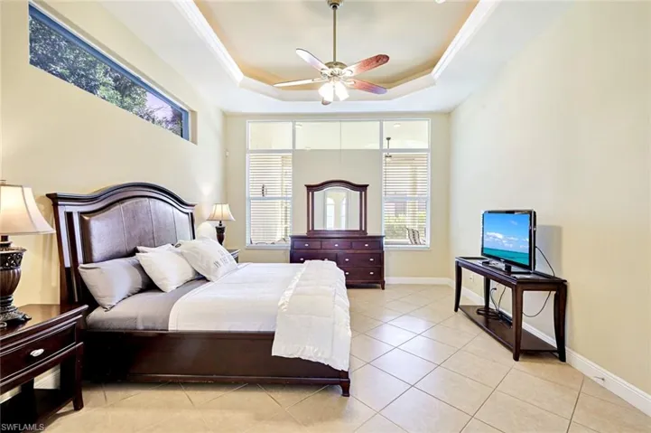 Bedroom with a tray ceiling, light tile patterned floors, a ceiling fan, and crown molding