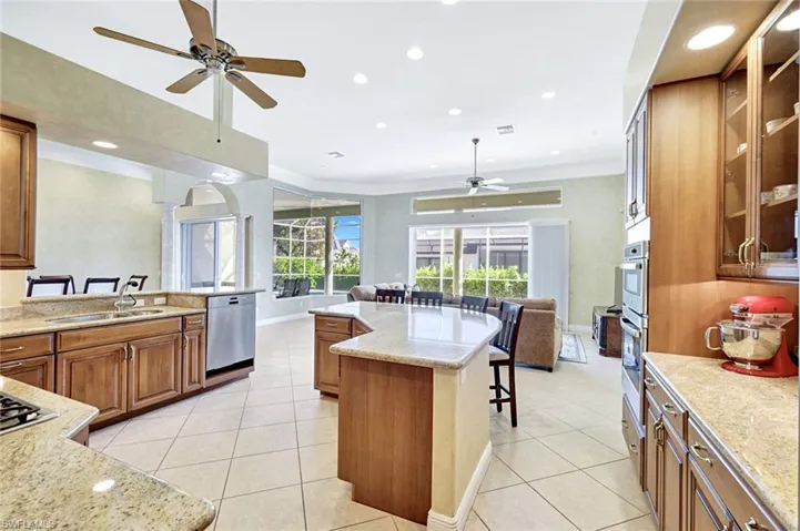Kitchen with brown cabinets, a kitchen bar, light stone counters, a ceiling fan, and open floor plan