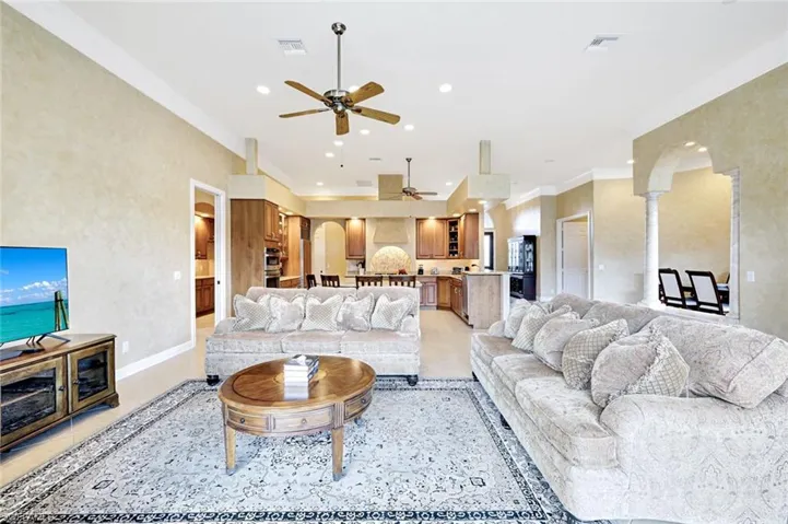 Living area featuring crown molding, arched walkways, recessed lighting, ceiling fan, and light tile patterned floors