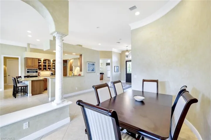 Dining room with crown molding, light tile patterned floors, ornate columns, recessed lighting, and arched walkways
