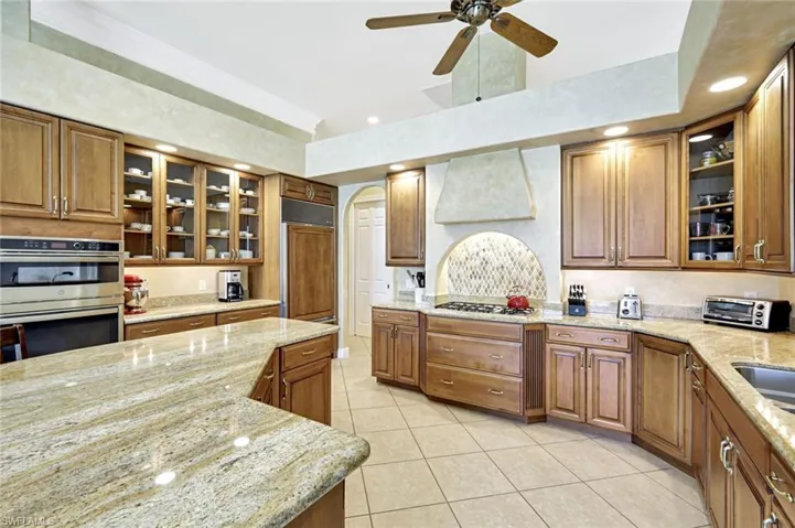 Kitchen featuring glass insert cabinets, brown cabinets, recessed lighting, and ornamental molding