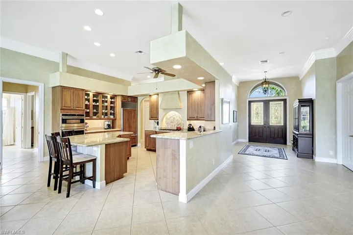 Kitchen featuring a breakfast bar area, ornamental molding, light stone counters, glass insert cabinets, and brown cabinets