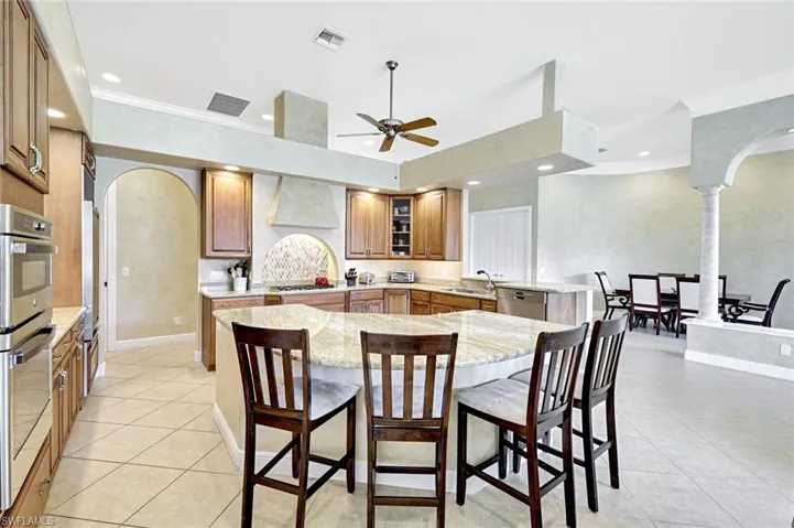 Kitchen featuring arched walkways, a peninsula, appliances with stainless steel finishes, brown cabinets, and ornamental molding