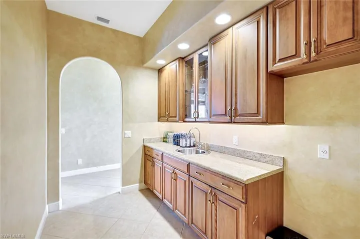 Kitchen featuring brown cabinetry, glass insert cabinets, arched walkways, light stone countertops, and light tile patterned floors