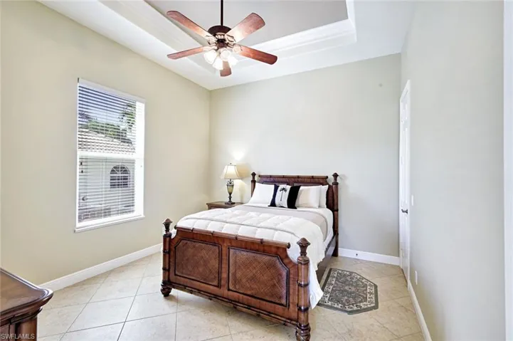 Bedroom with a tray ceiling, light tile patterned floors, and ceiling fan