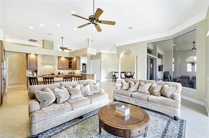Living area with arched walkways, ceiling fan, ornamental molding, light tile patterned flooring, and recessed lighting