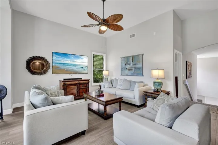 Spacious living area featuring a high vaulted ceiling, wood-finish flooring, a tropical-style ceiling fan, and a window with louvered blinds