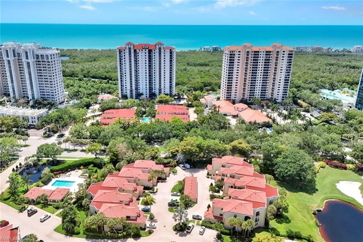 Aerial perspective showcasing multiple residential buildings with red tile roofs, surrounded by dense greenery and water features