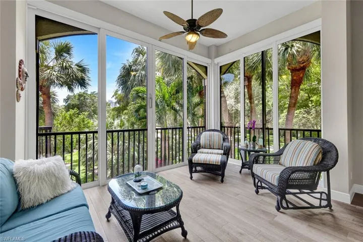Spacious sunroom featuring full-height sliding glass panels, light wood-finish flooring, and a ceiling fan with light fixture