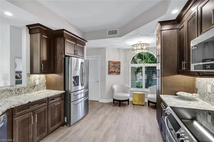 Gourmet kitchen featuring wood-finish flooring, dark wood cabinetry with crown molding, light-toned granite countertops, and stainless steel appliances