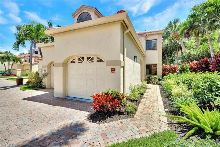 Stucco exterior featuring an arched garage door with decorative lites, a brick paver driveway, and a complementary brick paver walkway