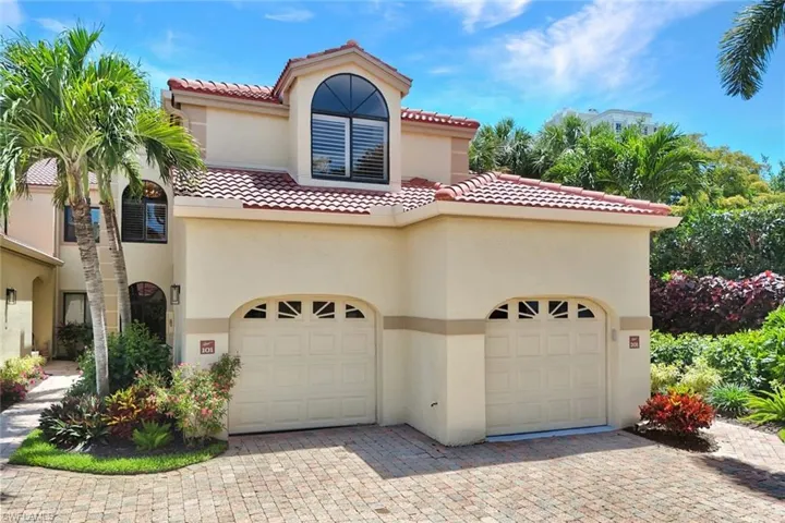 Mediterranean-inspired exterior featuring a two-car garage with arched entrances, a red tile roof, and a paver driveway