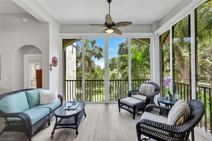Screened patio featuring wood-finish flooring, a ceiling fan with integrated lighting, and multiple sliding glass doors opening to tropical landscaping