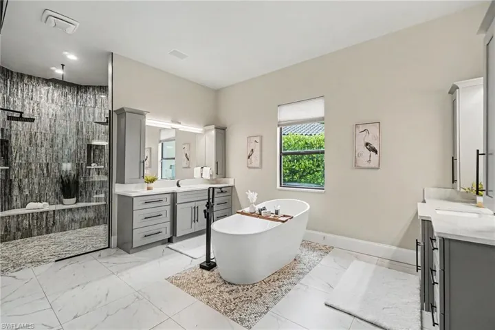 Spacious bath featuring a freestanding soaking tub, dual vanity with light gray cabinetry and white countertops, and a large walk-in shower with textured wall tile and a built-in bench