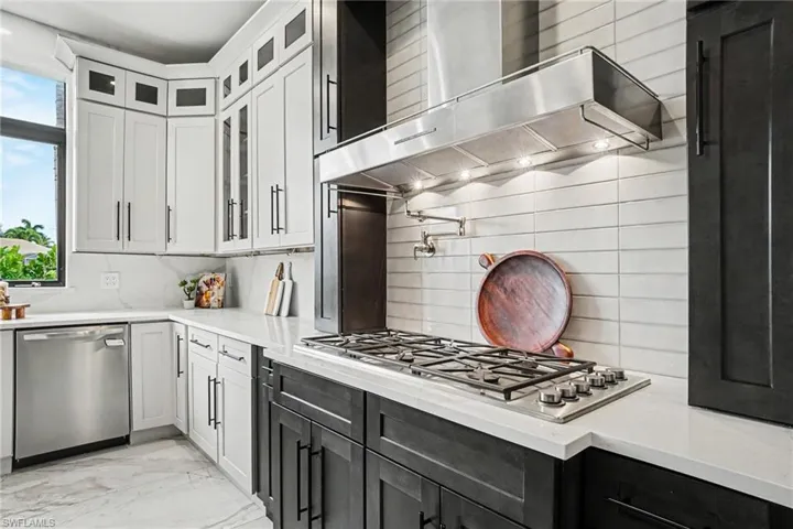 Contemporary kitchen featuring two-tone cabinetry, a stainless steel gas range with a pot filler, a matching stainless steel range hood, quartz countertops, and a full-height tile backsplash