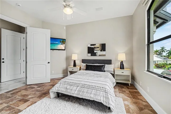 Neutral-toned bedroom featuring large format tile flooring, a ceiling fan with integrated lighting, and a window with black trim