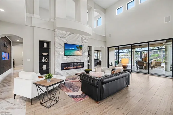 High-ceiling living area featuring a full-height stone-finish fireplace, built-in shelving, wood-finish flooring, and expansive sliding glass doors opening to an outdoor living space