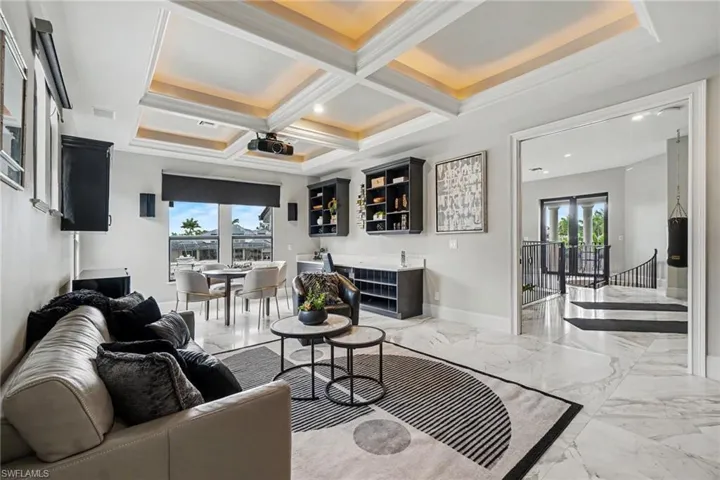 Coffered ceiling with recessed lighting, large format marble-look flooring, integrated media projector, built-in cabinetry, and expansive windows