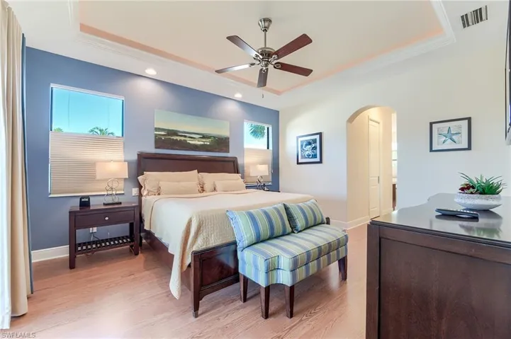 Bedroom featuring light hardwood / wood-style flooring, a raised ceiling, ceiling fan, and ornamental molding