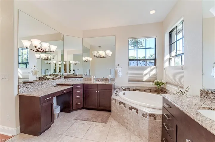 Bathroom with tile patterned flooring, vanity, a chandelier, and a relaxing tiled tub