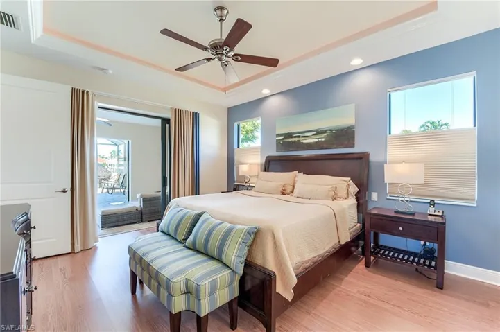 Bedroom featuring ceiling fan, access to exterior, light wood-type flooring, and a tray ceiling