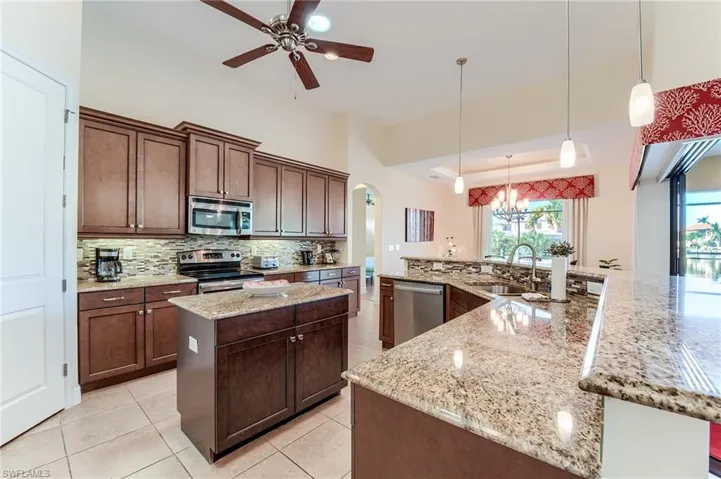 Kitchen with appliances with stainless steel finishes, light stone counters, a spacious island, sink, and decorative light fixtures