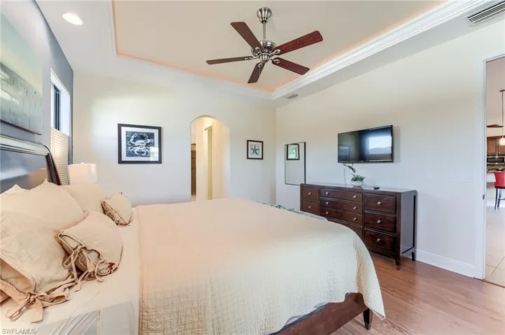 Bedroom with ceiling fan, a raised ceiling, light wood-type flooring, and ornamental molding