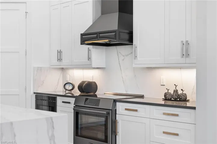 Kitchen with stainless steel range with electric stovetop, wall chimney range hood, white cabinets, and dark stone counters