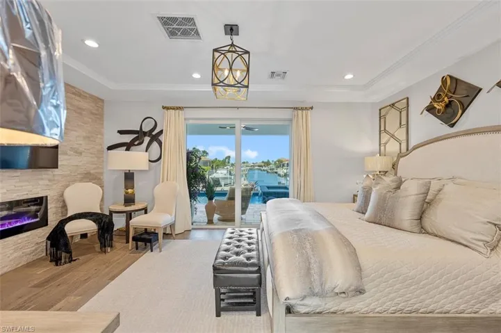 Bedroom featuring a water view, wood finished floors, recessed lighting, access to outside, and a glass covered fireplace