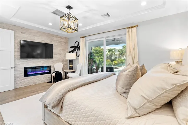 Bedroom featuring access to outside, light wood finished floors, a large fireplace, recessed lighting, and a raised ceiling