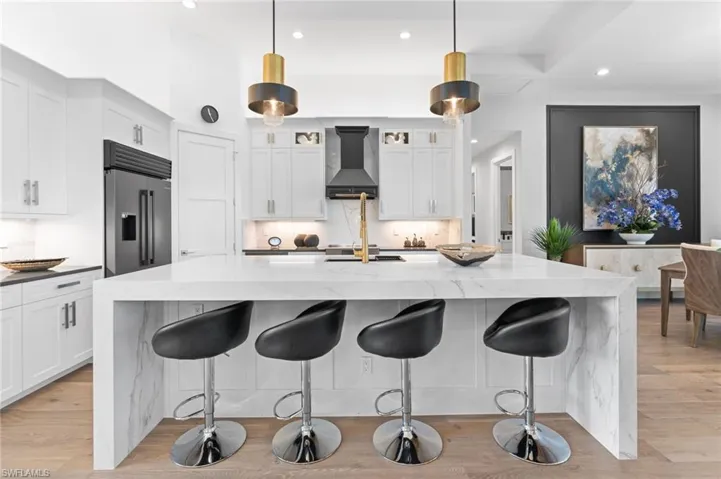 Kitchen with light stone countertops, recessed lighting, light wood finished floors, built in fridge, and pendant lighting