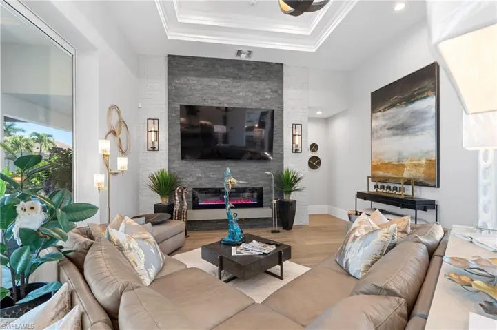 Living room with wood finished floors, a glass covered fireplace, crown molding, and a raised ceiling