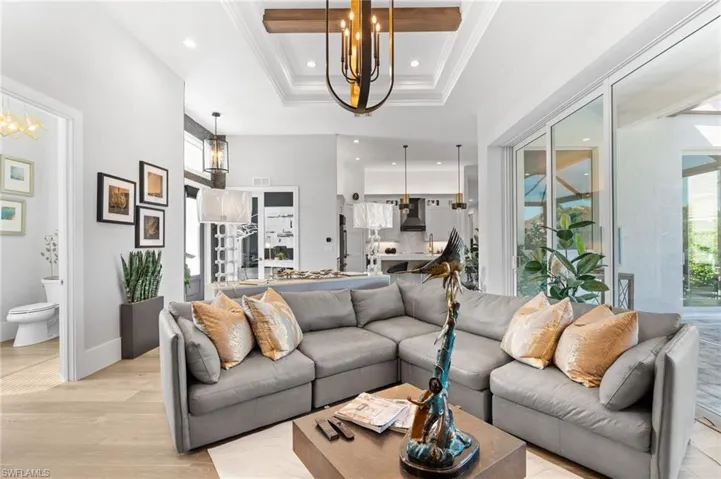 Living area featuring a chandelier, a tray ceiling, recessed lighting, light wood-style flooring, and crown molding
