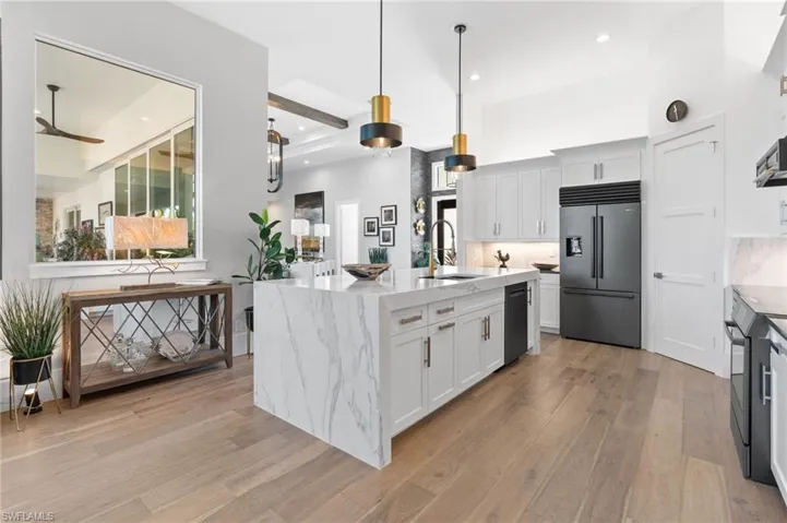 Kitchen featuring hanging light fixtures, white cabinets, light stone counters, a center island with sink, and recessed lighting