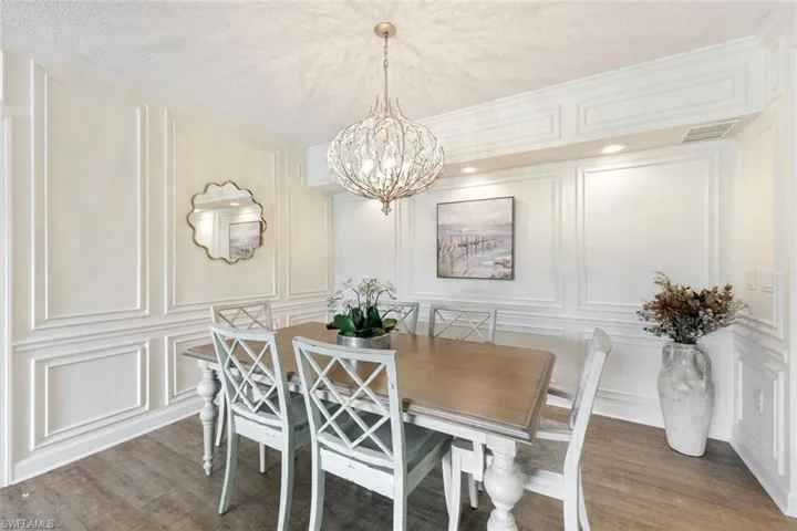 Dining room with a decorative wall, suspended lighting, light wood-type flooring, a textured ceiling, and ornamental molding