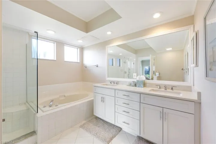 Full bath featuring double vanity, a stall shower, light tile patterned floors, a garden tub, and ornamental molding