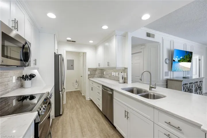 Kitchen featuring stainless steel appliances, light stone counters, white cabinetry, light wood finished floors, and a textured ceiling